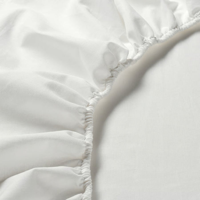 Close-up of a white fitted sheet with elasticized edges on a bed.