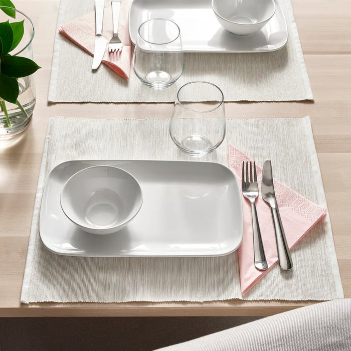 Dining table setting with white plates, bowls, and cutlery on a wooden surface.