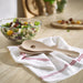 Wooden spoons on a white towel with a salad in the background