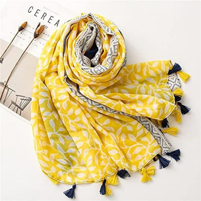 Digital Shoppy shawl scarf – yellow and white leaf print scarf with geometric border and tassels, laid flat on magazine

