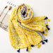 Digital Shoppy shawl scarf – yellow and white leaf print scarf with geometric border and tassels, laid flat on magazine

