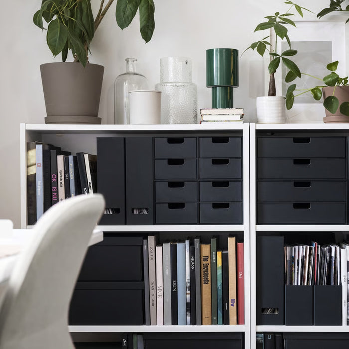White bookshelf with black drawers and books, decorated with plants and vases.