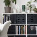 White bookshelf with black drawers and books, decorated with plants and vases.