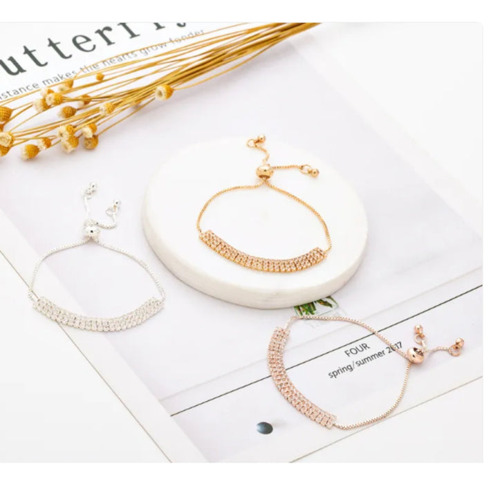 Three gold bracelets on a white surface with a magazine underneath