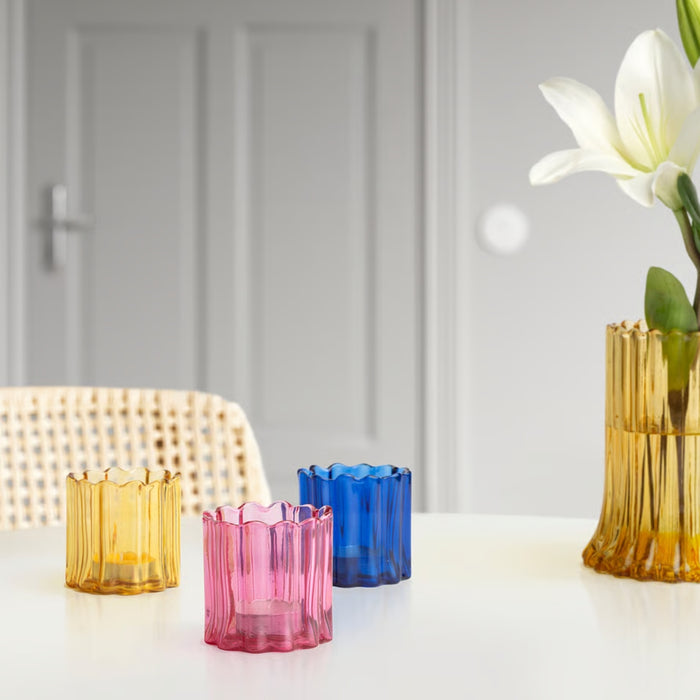 Colorful glass candle holders on a white surface with a blurred background