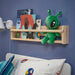 Green alien plush toy with antennae and expressive eyes placed on a wooden shelf among colorful children’s books in a space-themed bedroom with blue walls and playful décor.