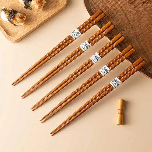 Set of wooden chopsticks with decorative handles on a beige surface.