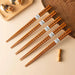 Set of wooden chopsticks with decorative handles on a beige surface.