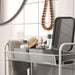 Bathroom vanity setup with a metal mesh shelf holding a gray tray with toiletries, including a pump dispenser bottle, wooden hairbrush, and small cosmetics—enhancing organized storage in a modern bathroom.-20599149