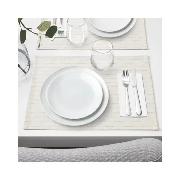 Dining table setting with white plates, glasses, and cutlery on a placemat.