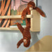 Two orangutan plush toys playfully hanging from a wooden shelf with colorful children’s books in the background.


