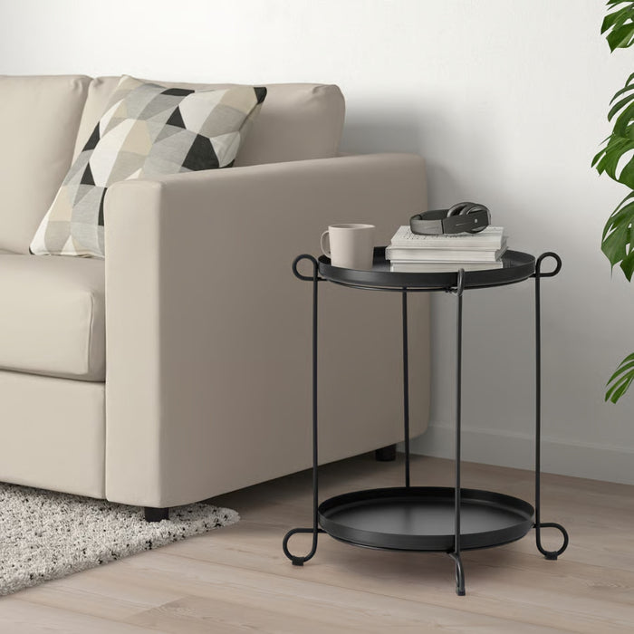 Black side table with a cup, books, and headphones next to a beige sofa in a living room.