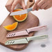 Three colorful Peeling Fruit Knifes on a wooden cutting board with an orange being sliced.