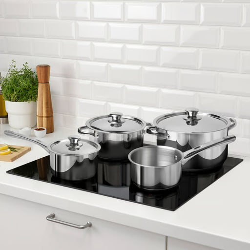 Set of stainless steel cookware on a kitchen counter with a white tiled wall background.