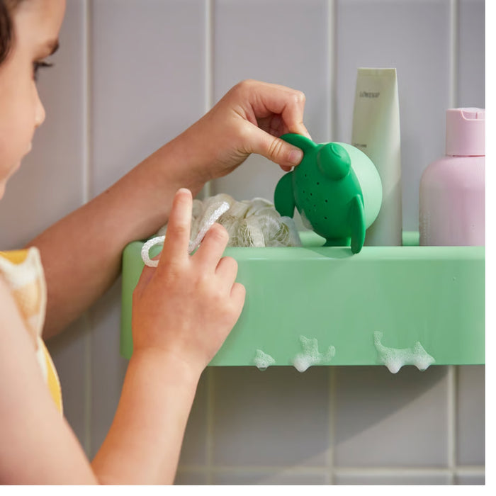 Child-friendly bathroom setup with HUMLESJÖN basket in light green, placed beside colorful hooks and accessories.

