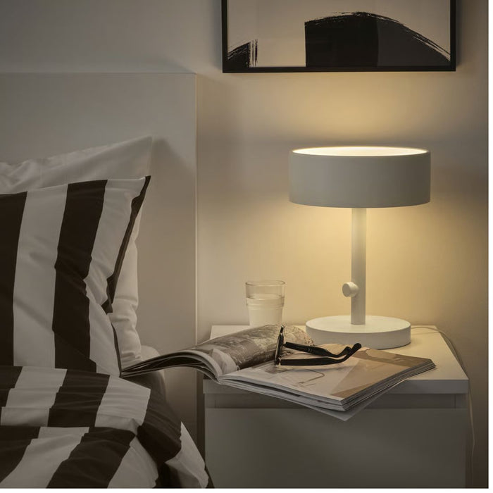 Modern bedroom with a bed, lamp, and magazine on a nightstand.