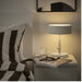 Modern bedroom with a bed, lamp, and magazine on a nightstand.
