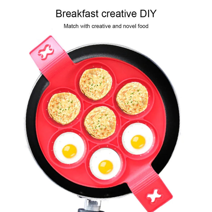 Red silicone 7-hole pancake and egg mold placed inside a black frying pan, filled with a mix of sunny-side-up eggs and golden brown vegetable patties. The compartments hold the food neatly, demonstrating creative breakfast possibilities. Text at the top reads: “Breakfast creative DIY” and “Match with creative and novel food.” Ideal for innovative cooking and evenly portioned meals -2147192 13025440.