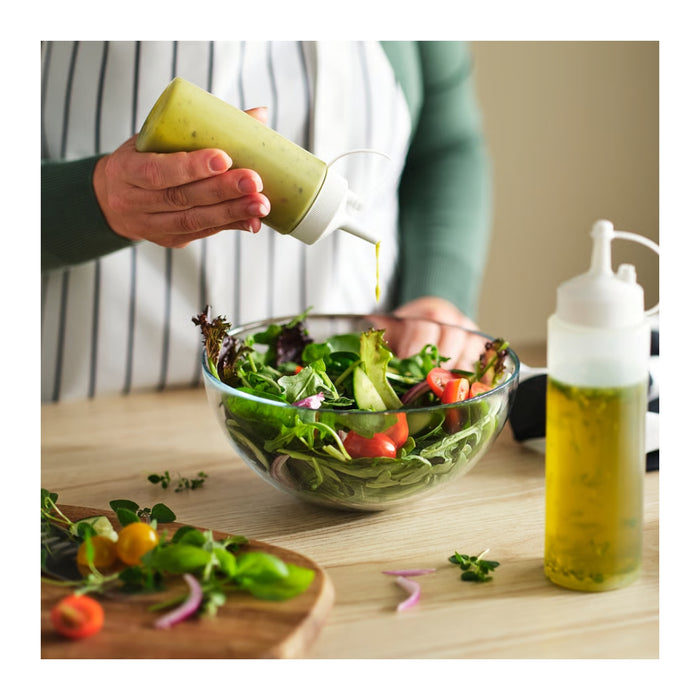 Person pouring dressing from a bottle onto a salad on a wooden table.