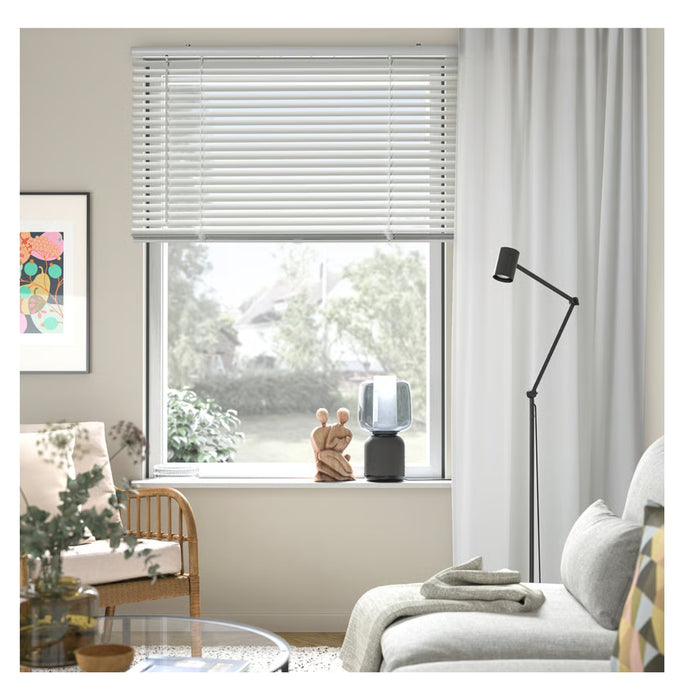 Living room with a window featuring white blinds and curtains, a lamp, and a chair.