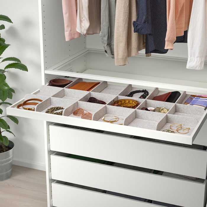 White dresser with open jewelry drawer and hanging clothes in the background