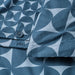 Detailed view of IKEA ÄNGSNEJLIKA fabric showing dark and light blue pinwheel-like geometric pattern with a sewn button and stitching, emphasizing craftsmanship and textile quality.

