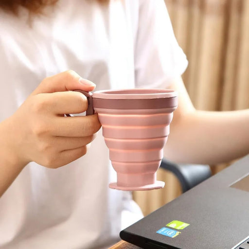 Person holding a pink collapsible mug with a blurred background