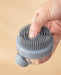 Gray silicone scrubbing brush with flexible bristles and a transparent liquid reservoir. Designed for bath and body cleansing, enabling deep exfoliation while dispensing soap or shampoo through the built-in container- 159845334888512362182