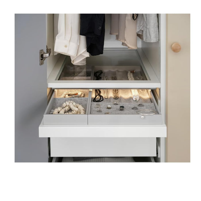 KOMPLEMENT jewelry drawer insert with compartments holding bracelets, rings, and necklaces, illuminated by built-in wardrobe lighting