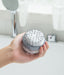 Gray silicone scalp massager with soft bristles, covered in foam, held in a hand for demonstration. Designed for shampoo application and gentle scalp massage to enhance cleansing and improve circulation. Showerhead and faucet in the background indicate use in a bathroom setting- 159845334888512362182