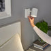 Hand adjusting a wall-mounted light fixture on a gray wall.