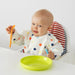 Baby in a high chair with a bib, plate, and utensils on a white background