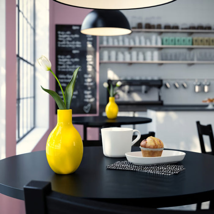 Yellow vase with a flower on a black table in a kitchen setting