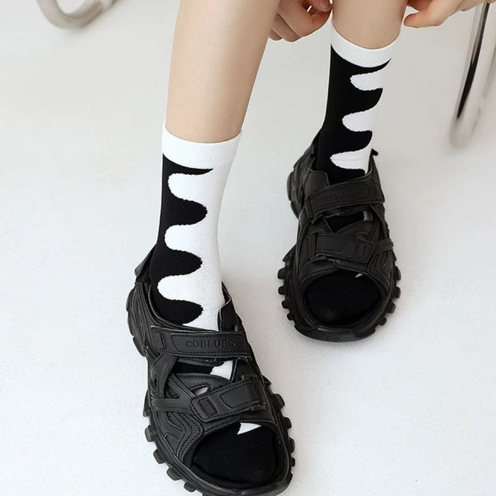 Close-up of feet in black sandals and white socks with abstract black wave pattern