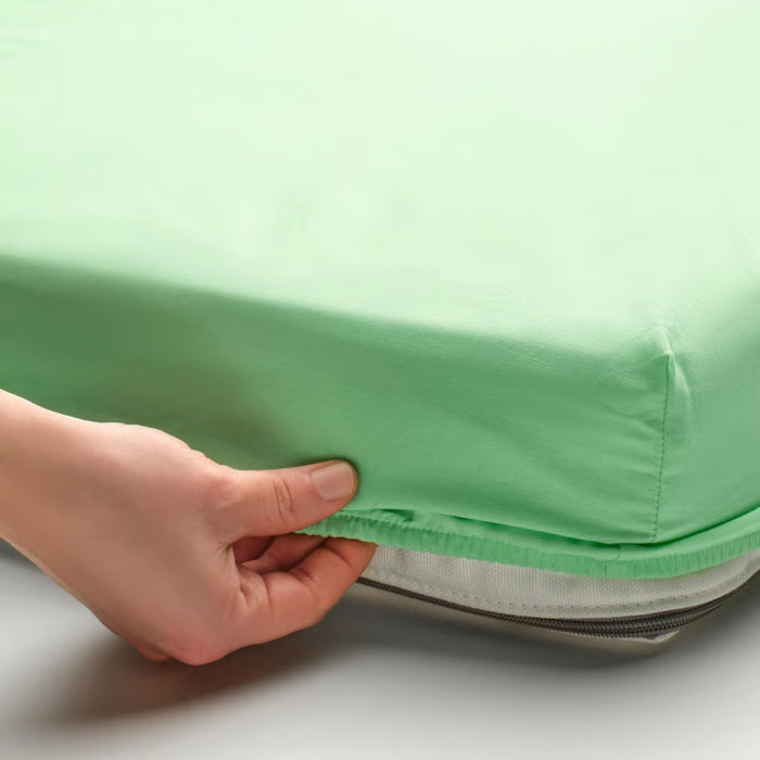 Person adjusting a green fitted sheet on a bed