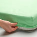Person adjusting a green fitted sheet on a bed