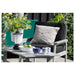 Outdoor seating area with a black cushioned chair, gray pillow, and small table with decorative items on a patio.
