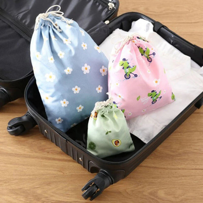 Open suitcase with three fabric drawstring bags, including blue floral, pink frog, and green avocado designs – 1598445710448 14078092