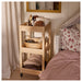  LOSHULT trolley beside bed in bedroom, top shelf with lotions and pouch, middle shelf with woven basket, bottom shelf with folded clothes, styled with striped bedding and floral pillows