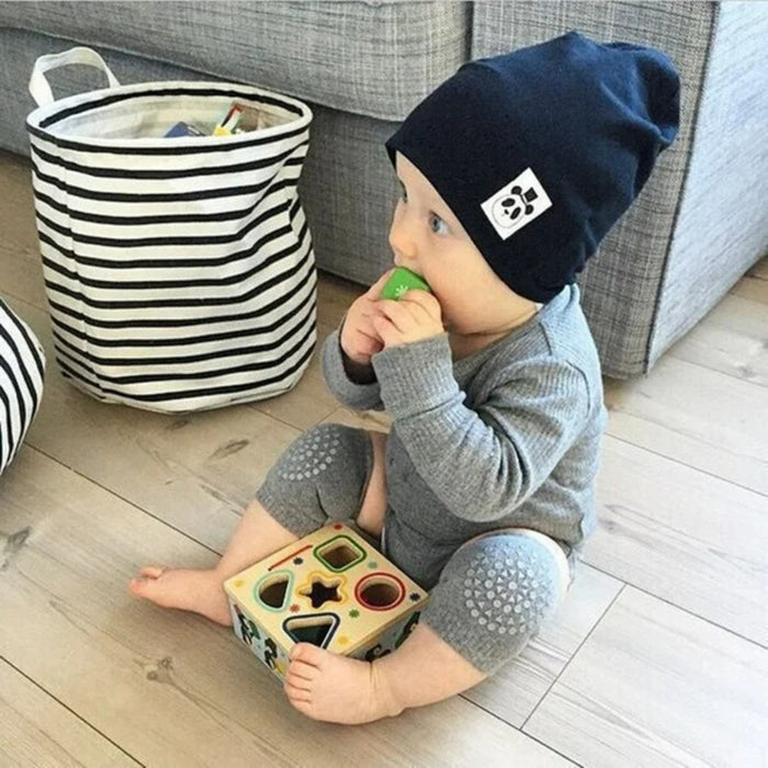 Baby anti-slip knee pads – toddler in grey outfit with patterned knees playing with shape-sorting toy