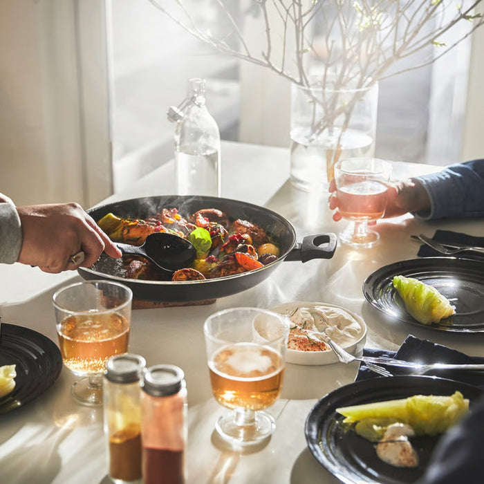 Dining table with a pan of food, glasses of beer, and plates with food.