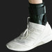 White athletic shoe with a black ankle support brace on a dark background