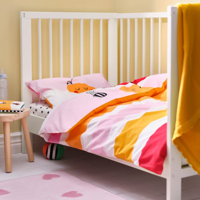 Children's bed with colorful bedding in a room with a yellow wall and pink rug.