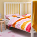 Children's bed with colorful bedding in a room with a yellow wall and pink rug.