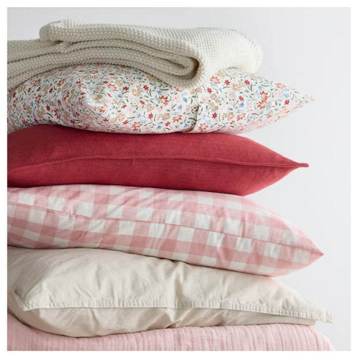 GULLNATTLJUS cushion cover, white/floral, 50x50 cm. Shown on top of stacked pillows with red, pink, and beige covers plus white knit blanket – 90598702.