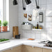 A modern kitchen setup featuring an IKEA SKÅDIS pegboard mounted on a white tiled wall. The pegboard holds various kitchen tools, including a pair of scissors, a grater, spice bottles, and a fabric pocket with essentials-60599519