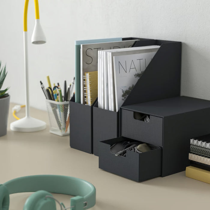 Black desk organizer with compartments on a desk with stationery items.