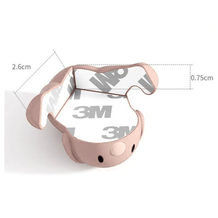 Pink silicone corner guard shaped like a cute puppy face, shown from the rear with peel-away adhesive pad exposed. The adhesive backing, branded with the 3M logo, measures 0.75 cm thick. The overall height of the corner guard is 2.6 cm. The design is both decorative and functional, ideal for protecting toddlers from sharp furniture edges -1600001888980 13025258.