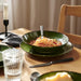 A bowl of pasta with tomato sauce served on a green IKEA PELARKAKTUS plate in a warm, homey dining setting.