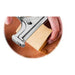 Hand using a cheese slicer to cut a block of cheese on a wooden board.